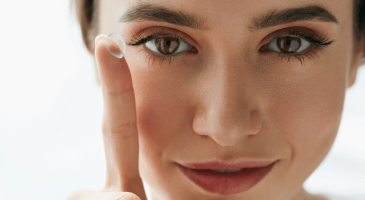 Woman holds contact lens on her finger.